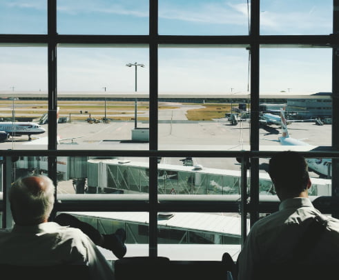 Two men waiting in airport terminal looking out to planes