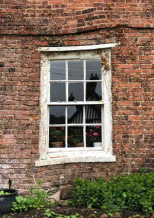Side of a house focused below the window showing cracks and a hole in the wall